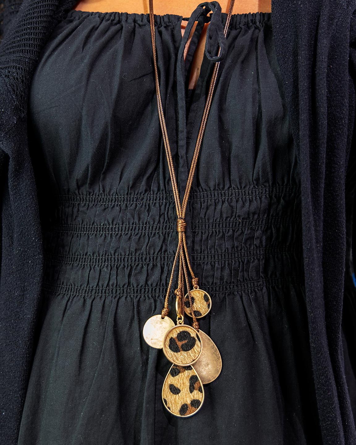 Long necklace with gold and leopard print pendants on a black outfit