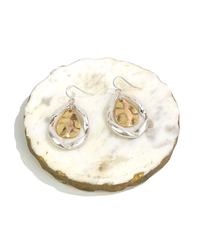 Teardrop-shaped earrings with gold and silver on a white stone surface