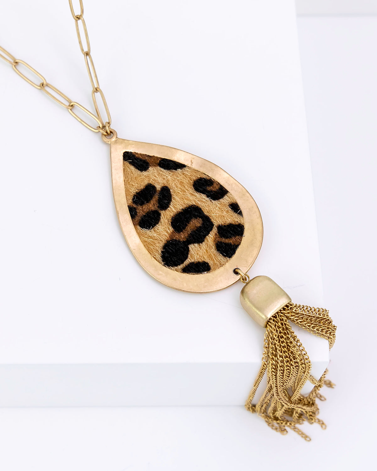 Necklace with a teardrop-shaped pendant featuring a leopard print design and a gold tassel on a white background.