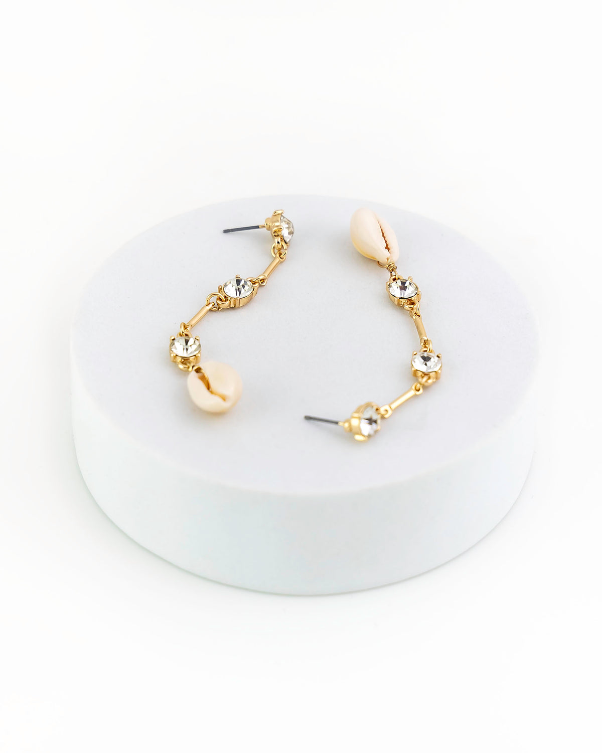 Gold and shell earrings on a white circular stand with a white background
