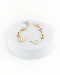 Gold and shell earrings on a white circular stand with a white background