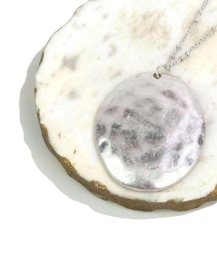 Silver necklace with a round pendant on a textured white surface
