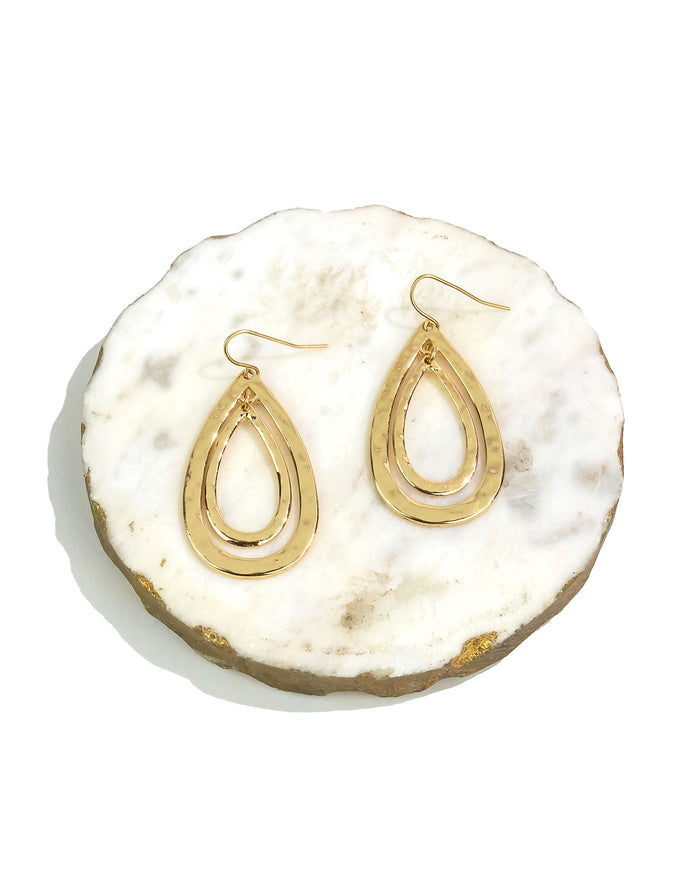 Gold teardrop earrings on a white and beige stone surface