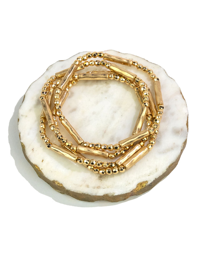 Stack of gold bracelets on a white marble surface