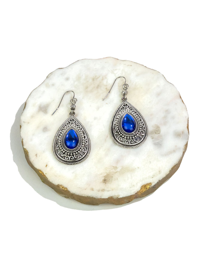 Pair of silver earrings with blue gemstones on a white stone surface
