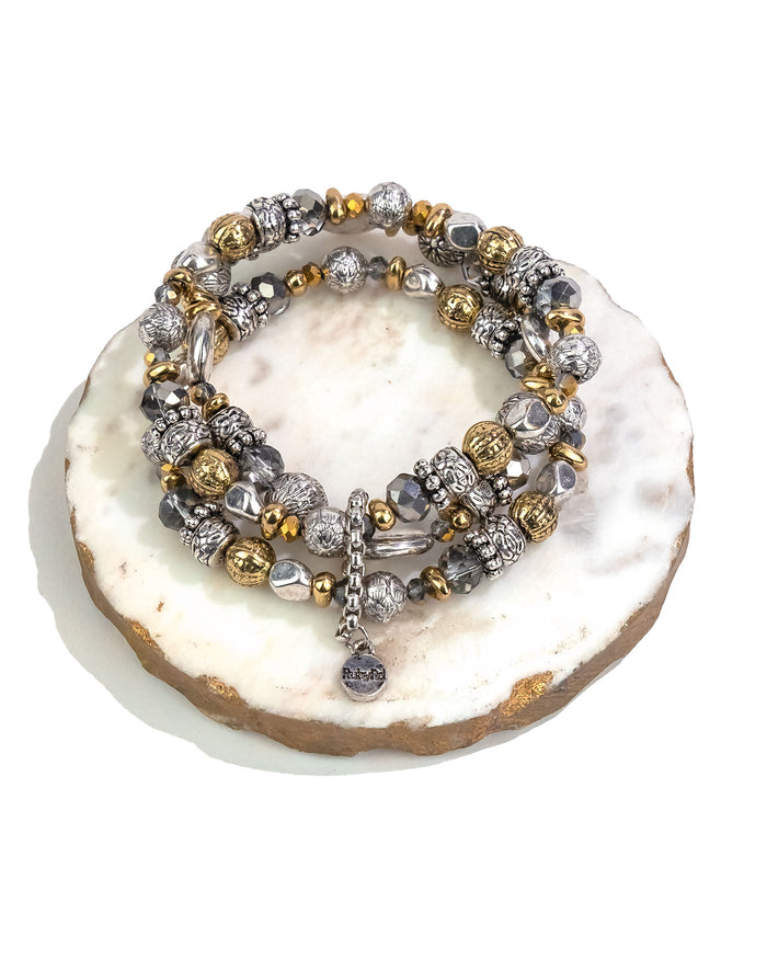 Stack of silver and gold-tone beaded bracelets on a white stone surface