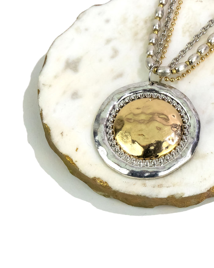 Close-up of a necklace with a gold and silver pendant on a white stone surface