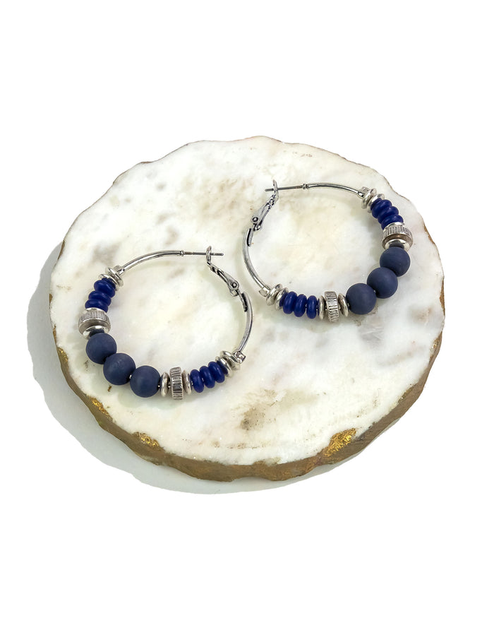 Pair of hoop earrings with blue beads on a white stone surface