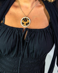 Person wearing a black top and gold necklace with a leopard print pendant.