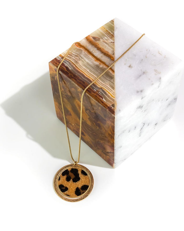 Gold necklace with a round pendant on a marble surface
