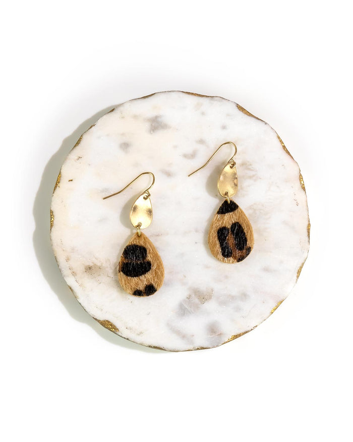 Pair of gold earrings with faux fur drops on a white marble surface