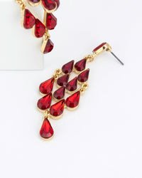 Gold chandelier earrings with red teardrop-shaped gemstones on a white background