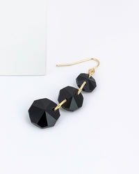 Close up of black faceted three drop earrings on a white background