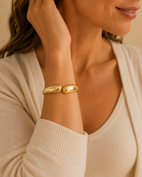 Model wearing a polished gold-tone sculptural bypass bangle with a neutral outfit.