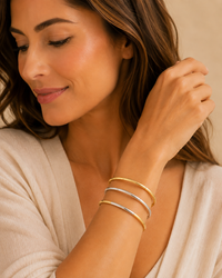 Model wearing a set of three slim two-tone gold- and silver-tone stretch bangles with an ivory blouse.