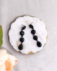 Black teardrop earrings on a white marble surface with a light gray background
