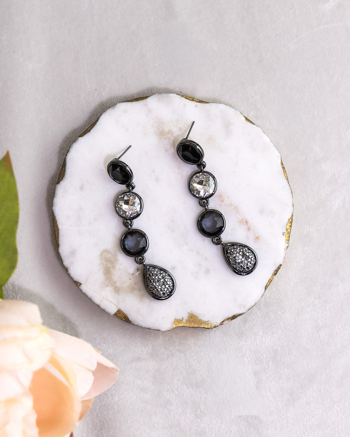 Black teardrop earrings with clear stones on a white stone surface