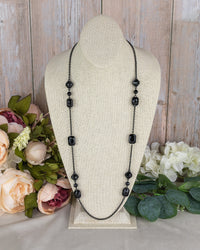 Black beaded necklace on a mannequin bust with flowers in the background