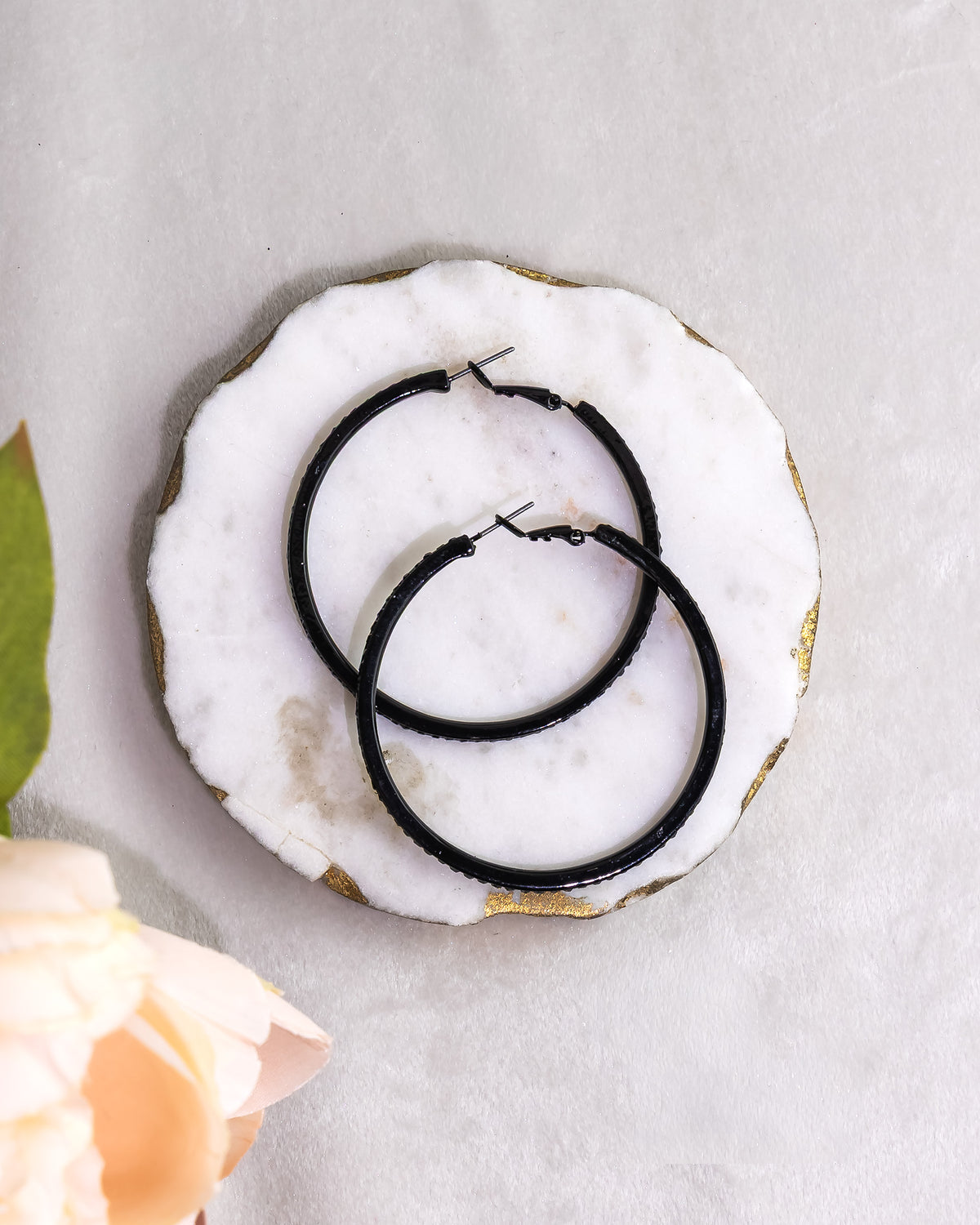Black hoop earrings on a white stone surface with a blurred flower in the background