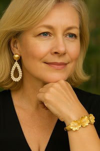 Woman wearing gold earrings and bracelet with a blurred green background