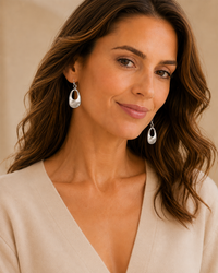 Model wearing worn-silver small open teardrop earrings with a neutral V-neck top.
