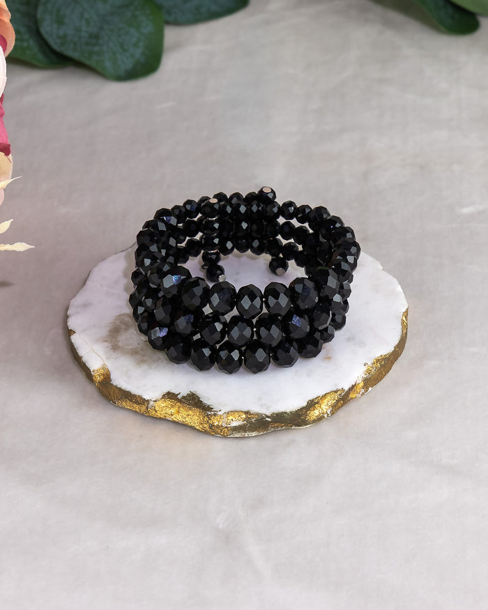 Black beaded bracelet on a white and gold coaster with green leaves in the background