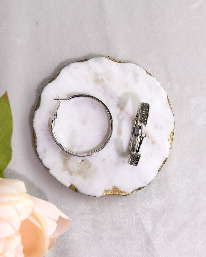 Silver hoop earring and black diamond stud earring on a white marble coaster with a light gray background.