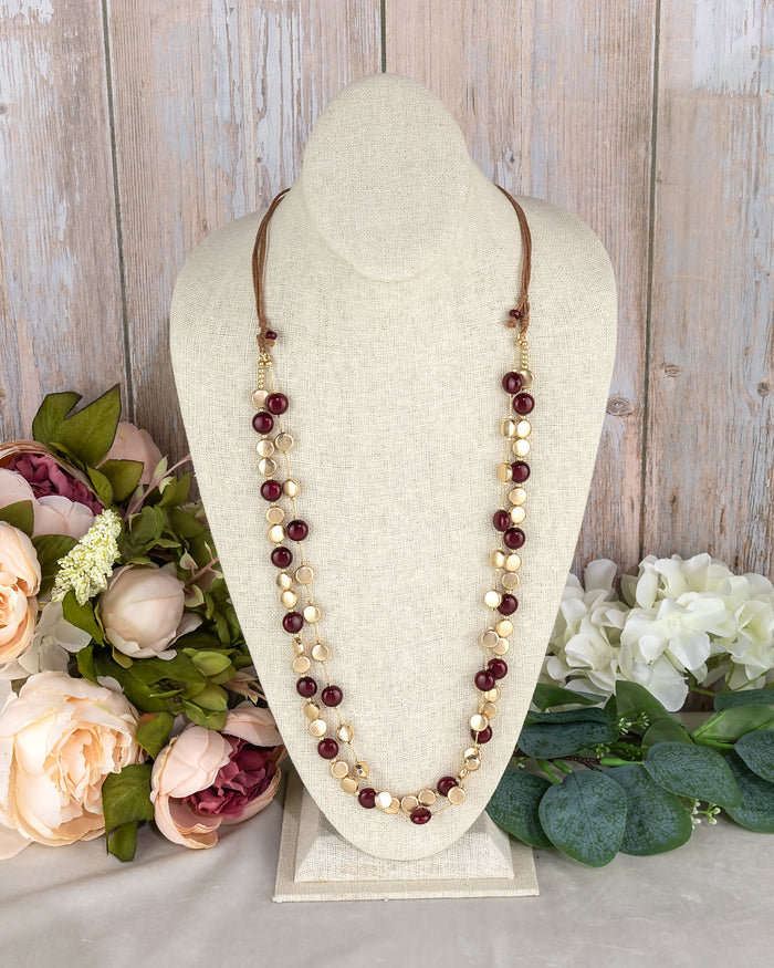Necklace with beads on a white stand with flowers in the background