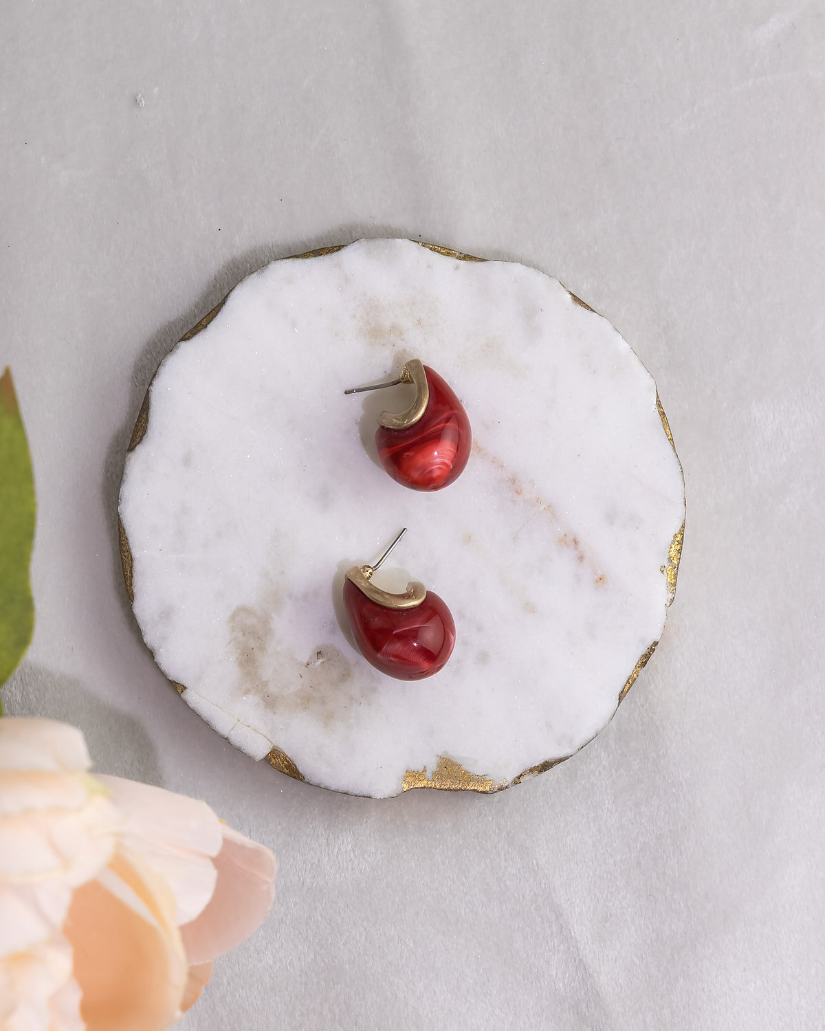 Red cherry-shaped earrings on a white marble surface with gold accents.