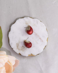 Red cherry-shaped earrings on a white marble surface with gold accents.