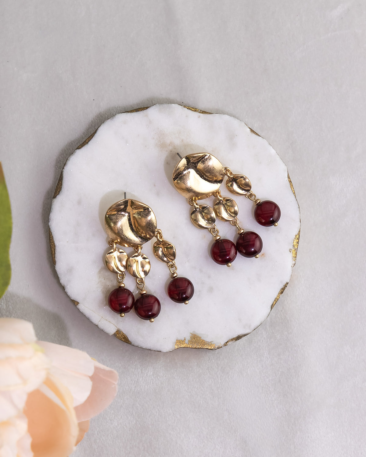 Gold earrings with red beads on a white stone surface