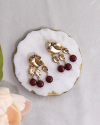 Gold earrings with red beads on a white stone surface