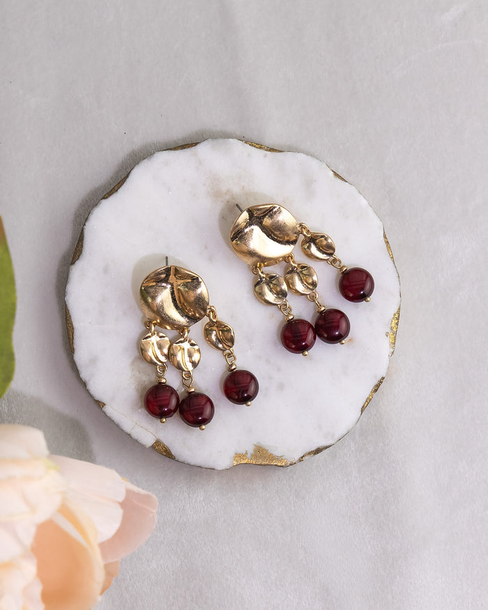 Gold earrings with red beads on a white stone surface