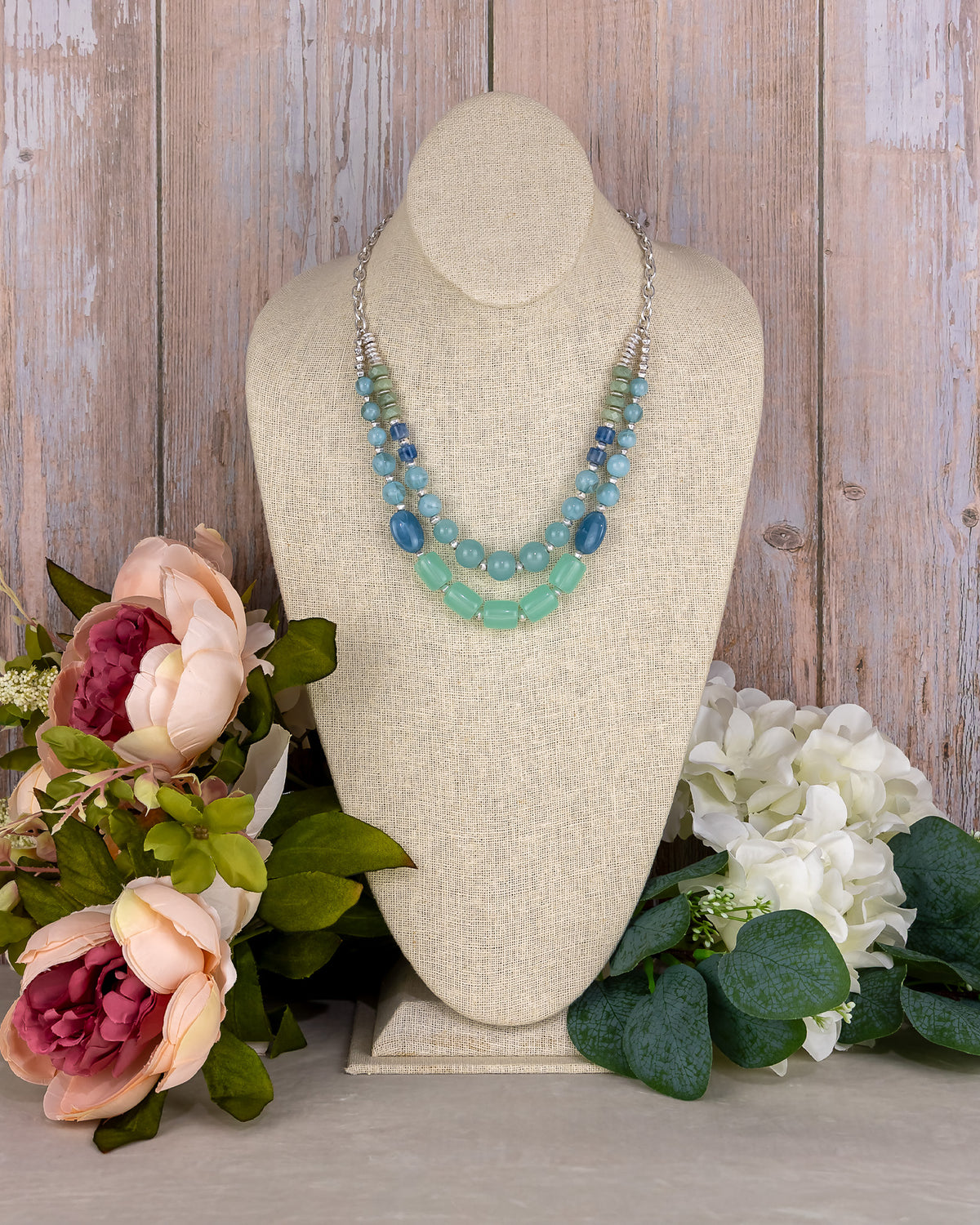 Necklace on a mannequin bust with flowers in the foreground against a wooden background
