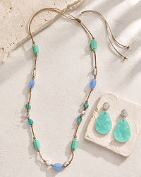 Necklace and earrings with turquoise and gold beads on a textured surface
