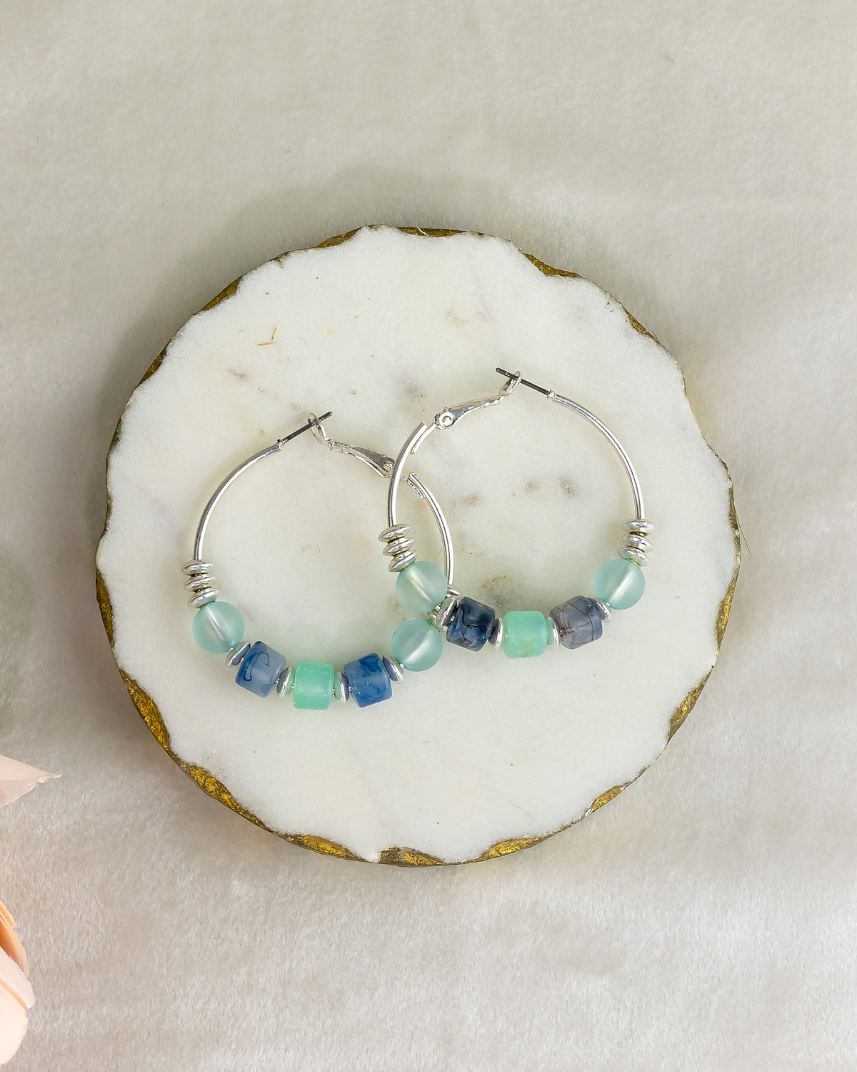 Silver hoop earrings with blue and teal beads on a white stone surface