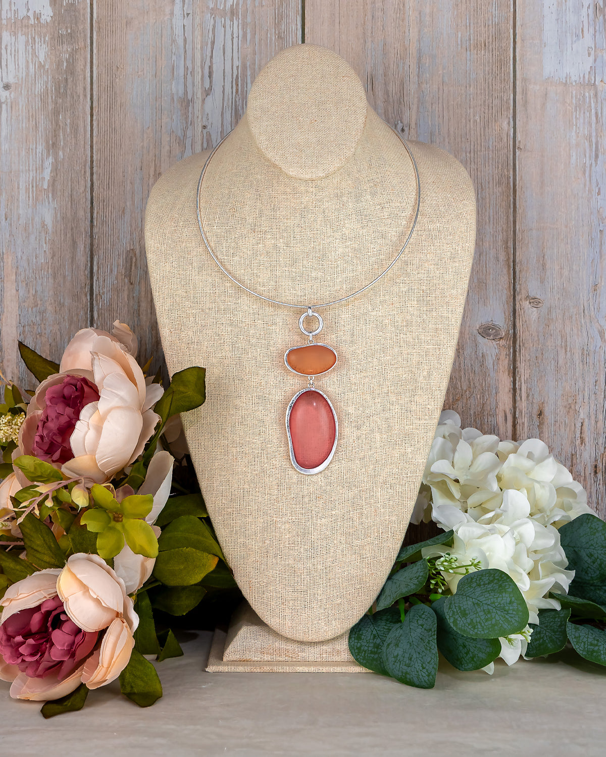 Necklace with pink and orange stones on a bust with flowers in the background