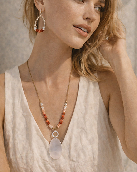 Woman wearing a necklace with a large pendant and matching earrings against a neutral background
