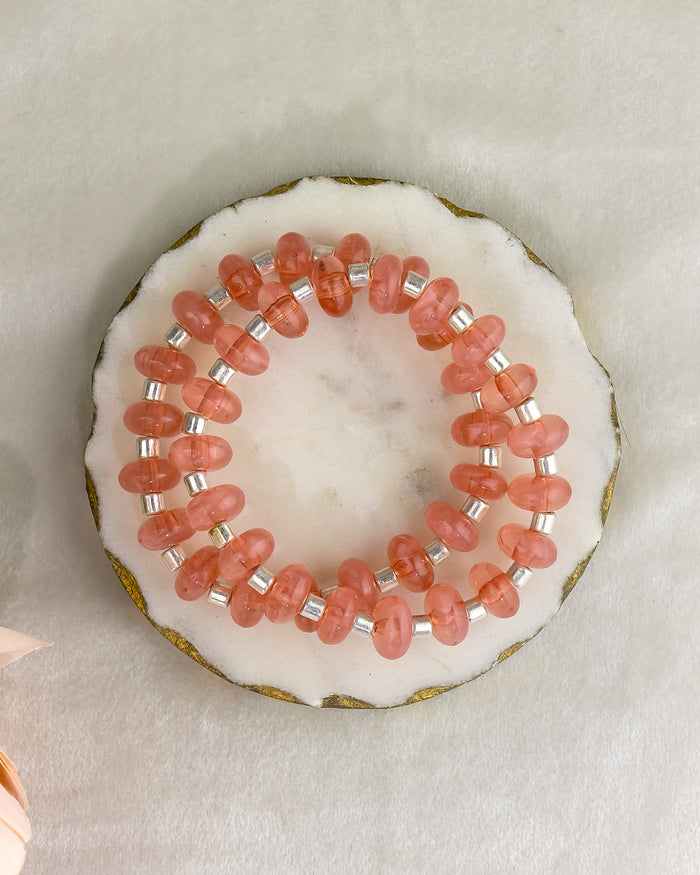 Two pink beaded bracelets on a white shell with a beige background