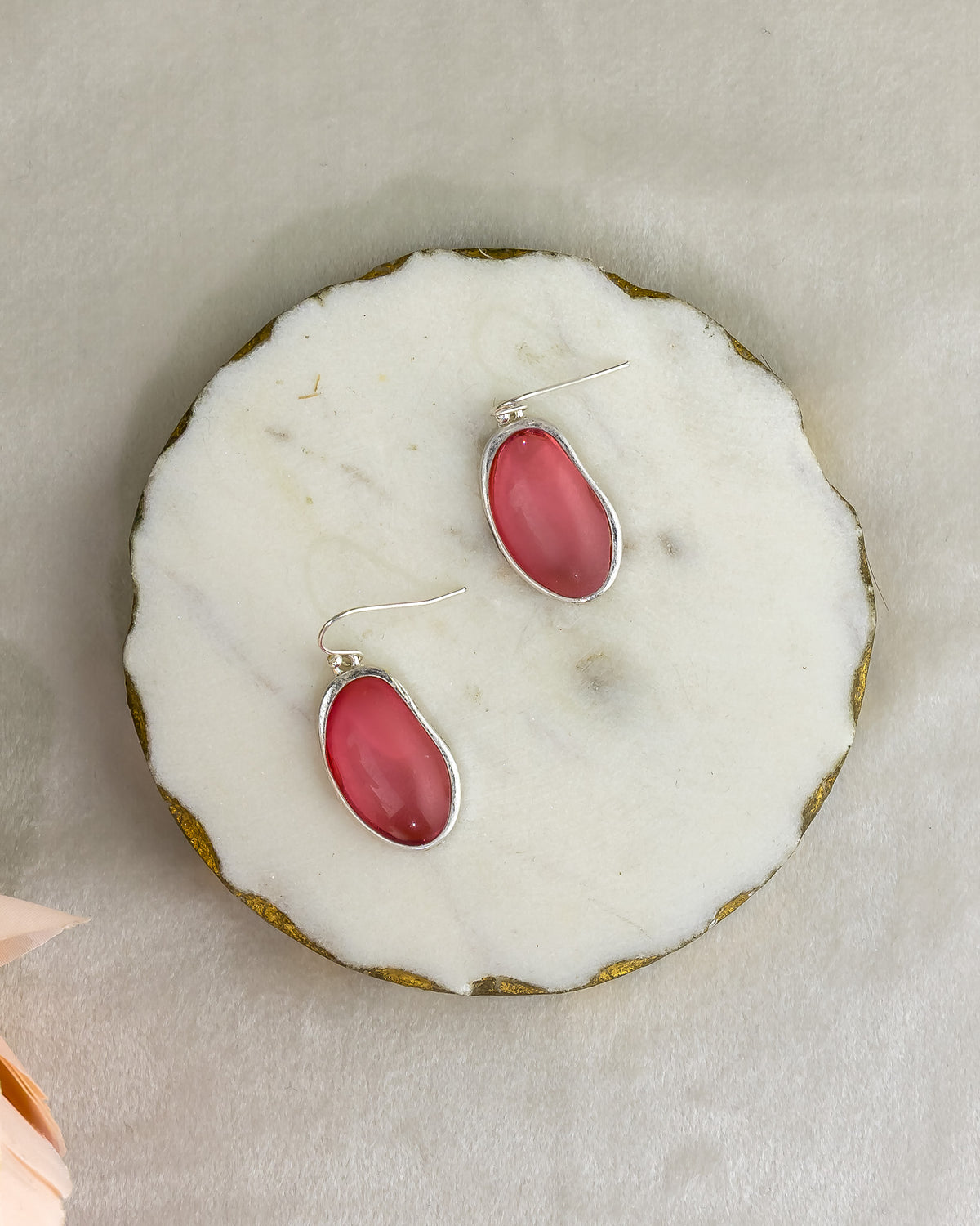 Pair of red earrings with silver hooks on a white marble surface