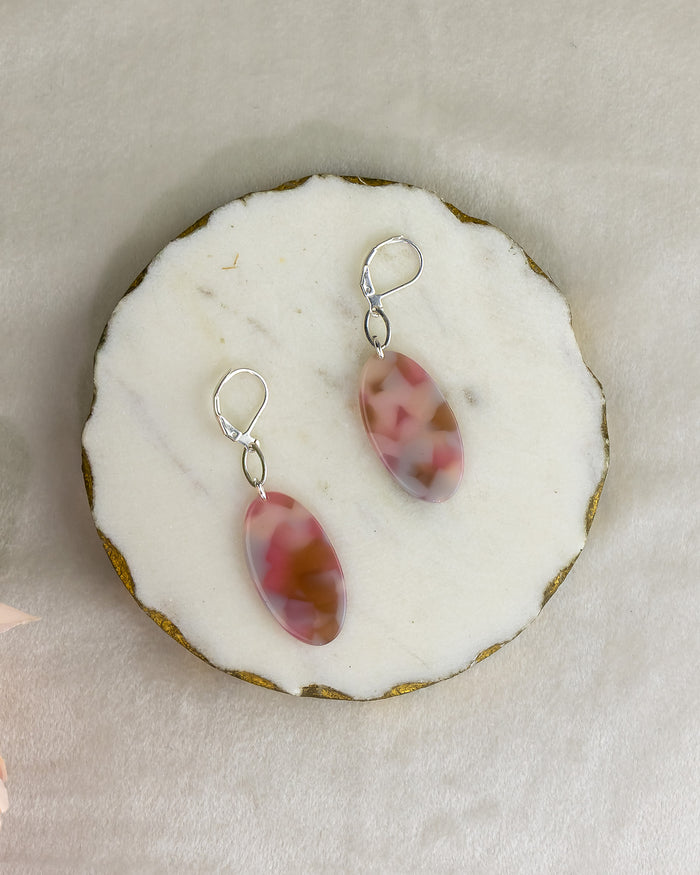 Pair of pink and red marbled earrings on a white stone surface