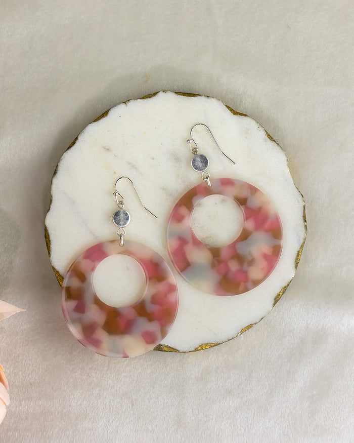 Pair of earrings with pink and white circular design on a white shell