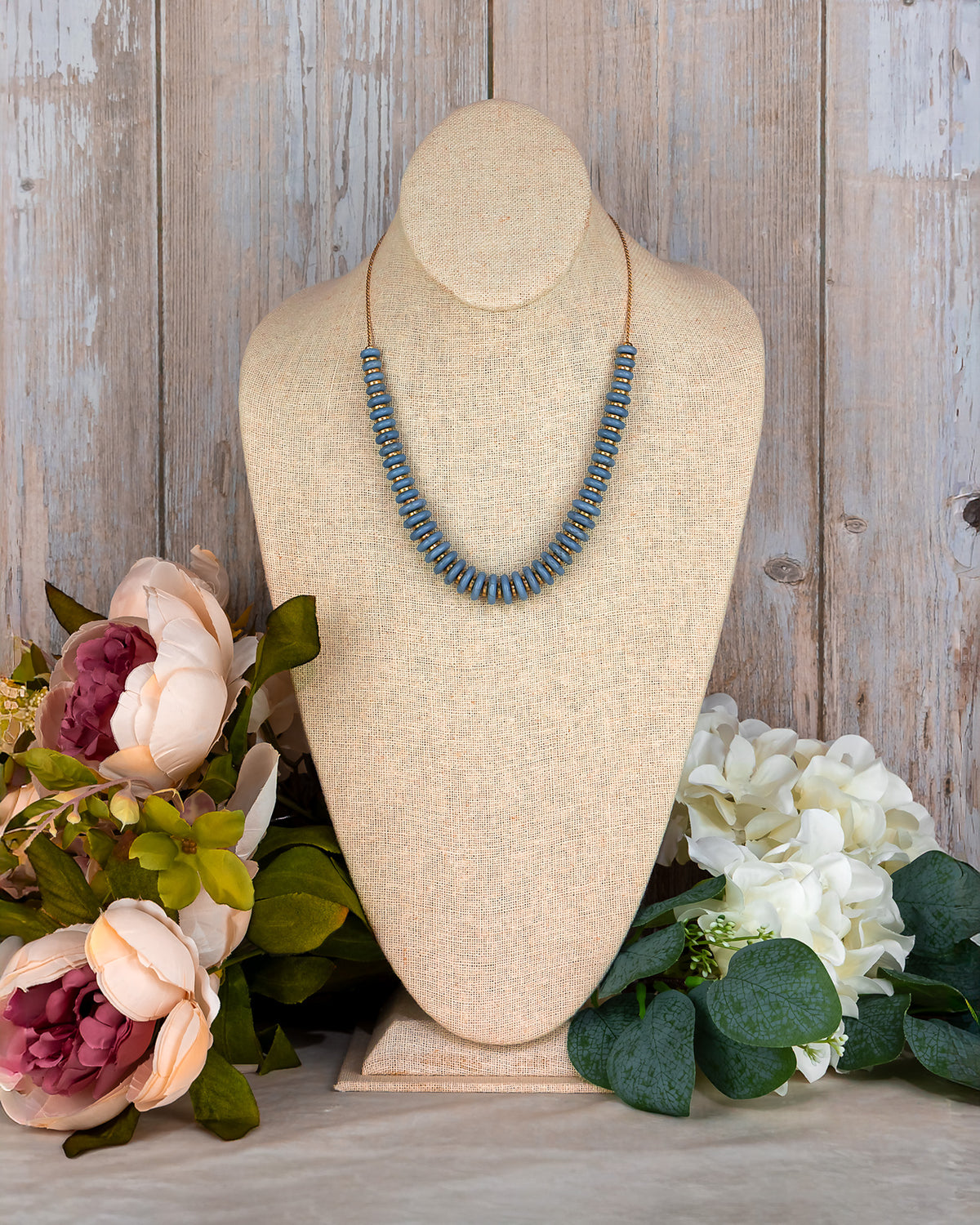 Necklace on a mannequin bust with flowers on a wooden background