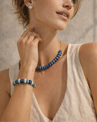 Woman wearing a blue beaded necklace and bracelet against a neutral background