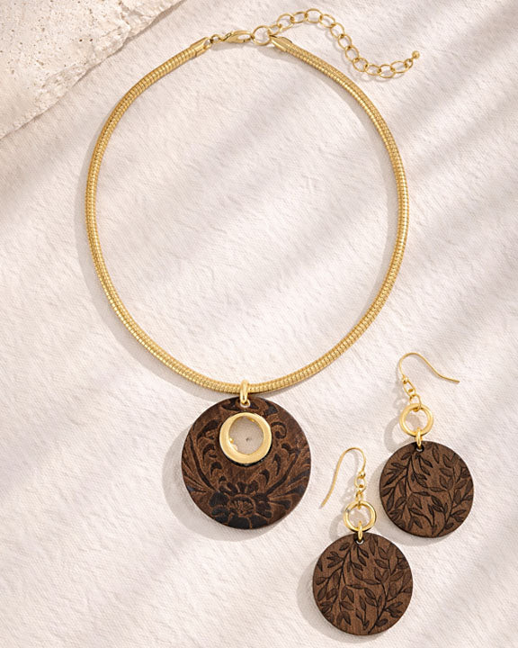 Gold necklace and earrings with brown circular pendants on a textured white surface