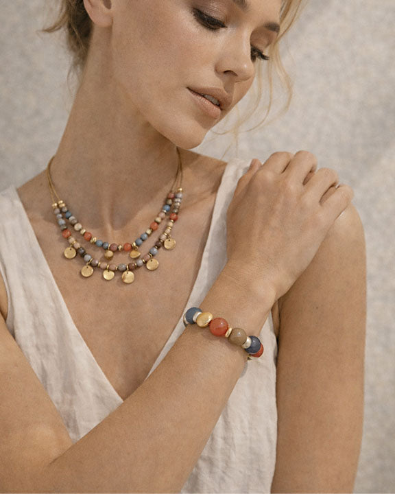 Woman wearing a colorful beaded necklace and bracelet against a neutral background