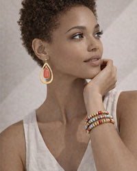 Woman wearing a gold earring and colorful bracelets on a neutral background