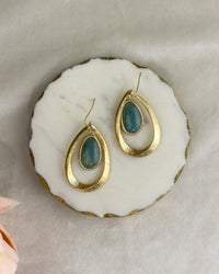 Gold earrings with blue stones on a white stone surface