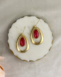 Gold earrings with coral stones on a white marble surface