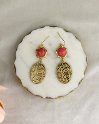 Pair of gold earrings with red stones on a white stone surface